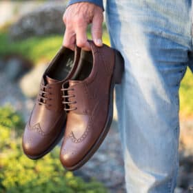 Man holding a pair of brown Will vegan shoes.